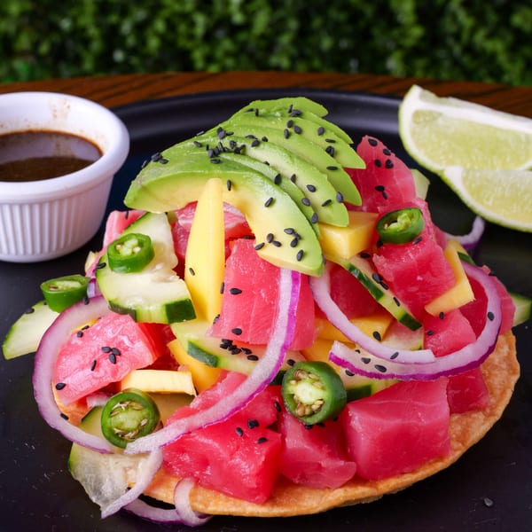 Tuna tostada with avocado, mango, red onion, jalapeño, and sesame seeds, with a side of sauce.