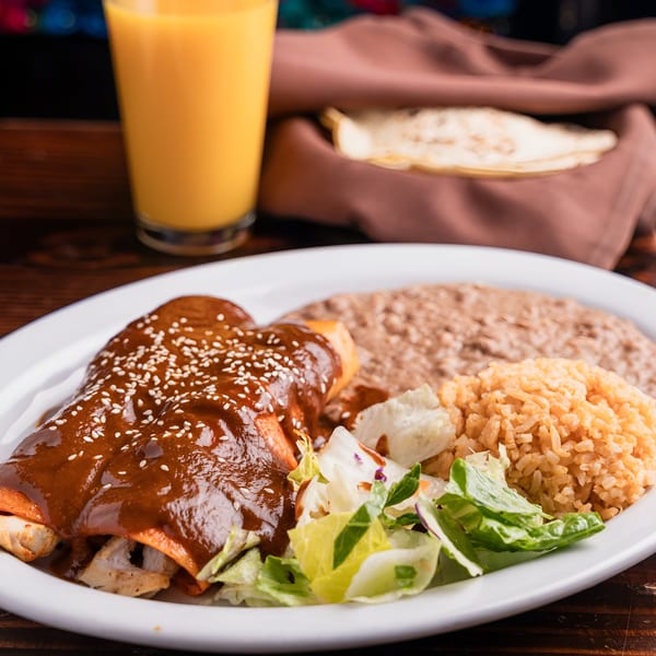El Tarasco's chicken enchiladas with mole sauce, rice, beans, and salad, with a drink and tortillas.