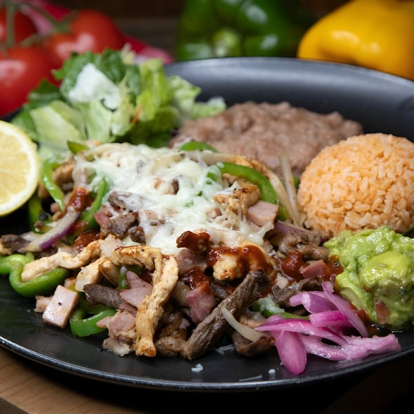 El Tarasco's sizzling fajitas with chicken, steak, peppers, onions, rice, beans, guacamole, and a lemon wedge.