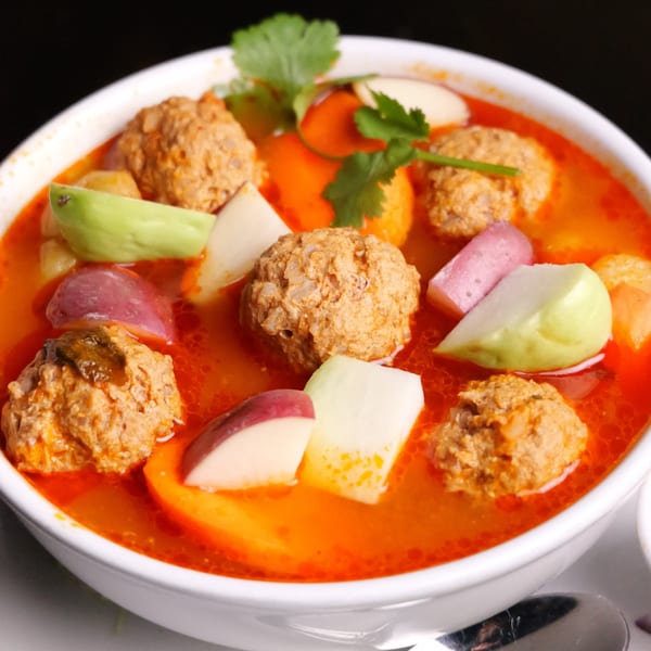 A vibrant bowl of Mexican meatball soup with vegetables and cilantro in a white bowl.