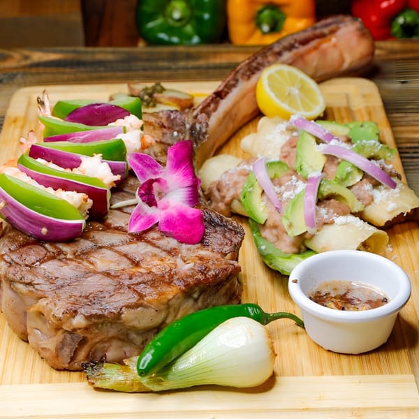 El Tarasco's Mexican steak and shrimp dish with enchiladas, avocado, onions, and a lemon slice.