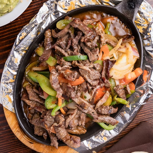 Sizzling beef fajitas with green and orange bell peppers and onions in a cast iron skillet.